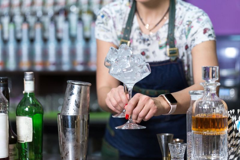 A professional bartender holds glasses with ice cubes in his hands.