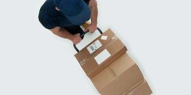 Delivery worker pushing a hand truck loaded with cardboard boxes.
