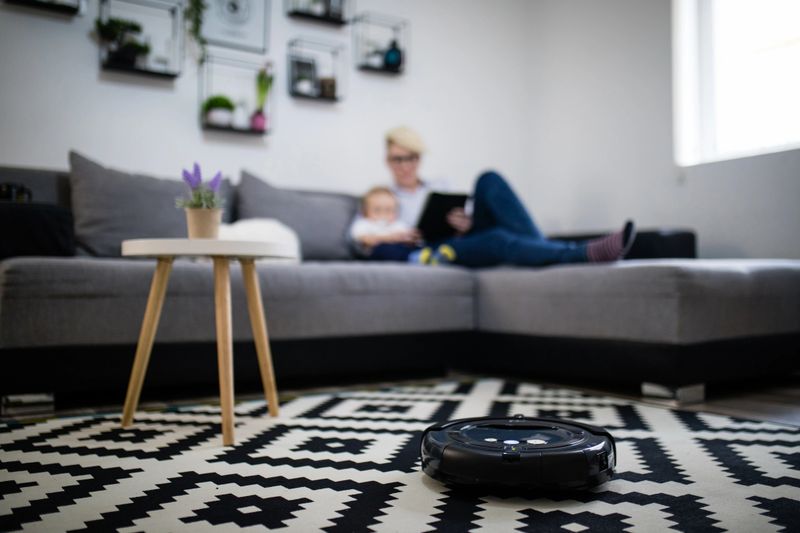 woman and boy using tablet while robot vacuum cleaning floor at home. Modern lifestyle concept.