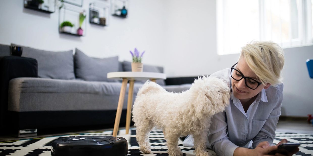 Person lying on floor with a small white dog in a modern living room.