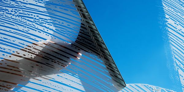 Hand using a squeegee to clean a soapy window under a blue sky.