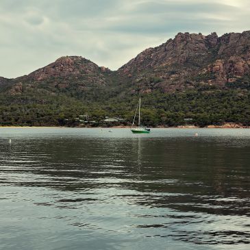 Sailboat floating on calm water with rocky hills in the background.