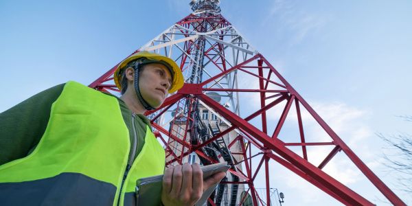 Construction worker with helmet and tablet near a telecom tower.