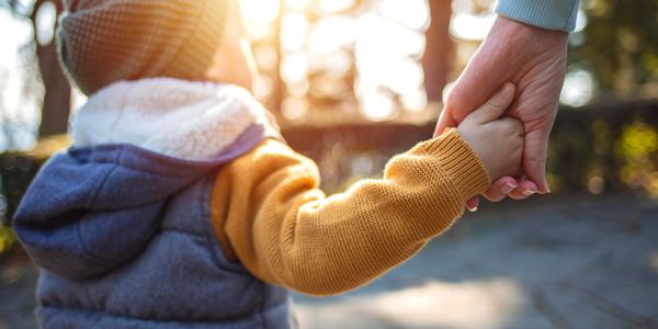 Child holding an adult's hand outdoors during sunset.