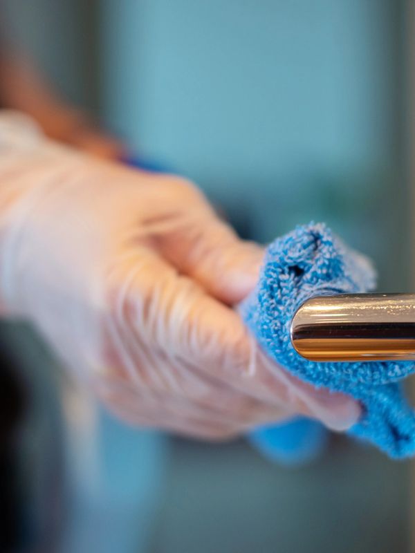 Person cleaning door handle with a blue cloth wearing gloves.