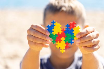 Child holding a colorful puzzle heart in front of their face.