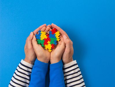 Demonstrating family support, hands holding a heart-shaped puzzle made of colorful pieces on a blue background.