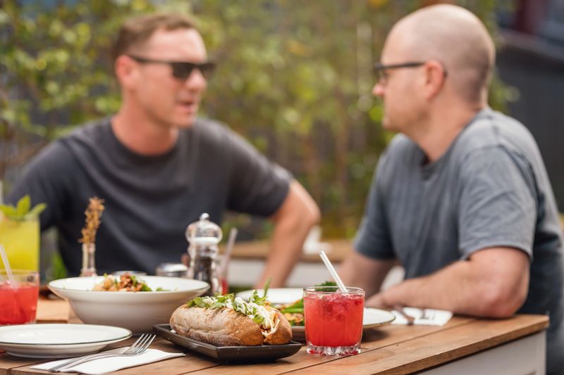 Male Friends Enjoying Healthy Summer Casual Lunch At Al Fresco Deli