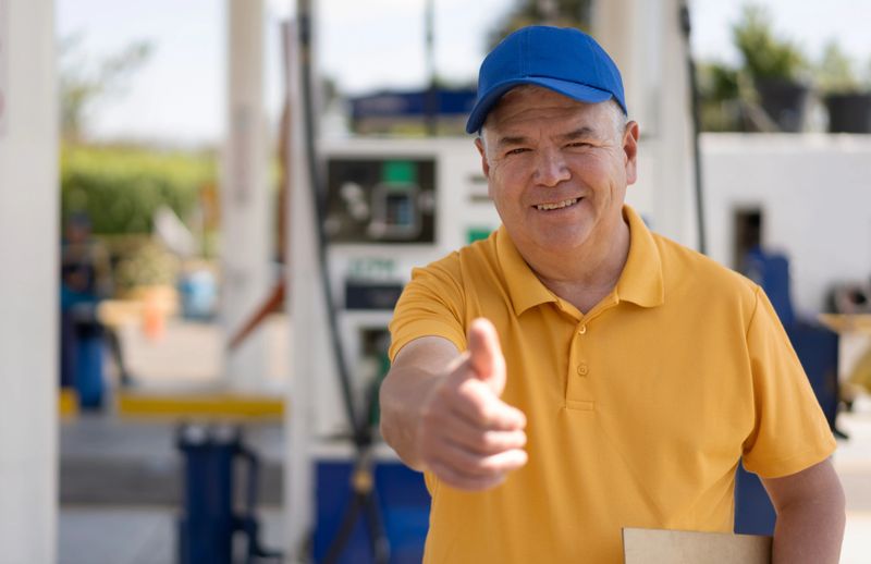 Friendly mature man working at a gas station facing camera smiling with thumbs up - Business concepts