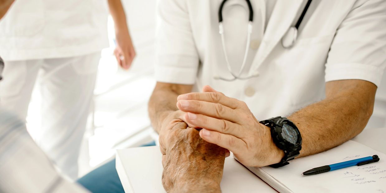 A doctor compassionately holds an elderly patient's hand during a consultation.