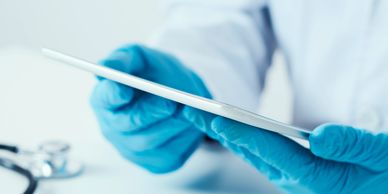 Healthcare professional wearing blue gloves using a tablet.