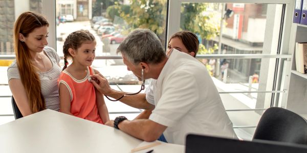 A doctor examines a young girl while her mother watches attentively.