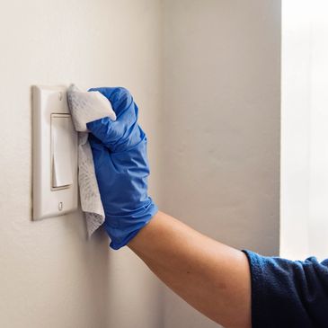 Gloved hand cleaning a light switch with a cloth.