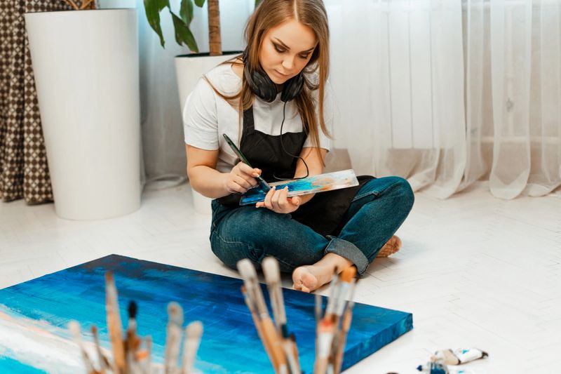 Art, the work of the artist. Young beautiful girl artist paints a picture and listens to music with headphones. Workshop of the artist. Drawing and music, paints. Inventory of the artist. Close-up