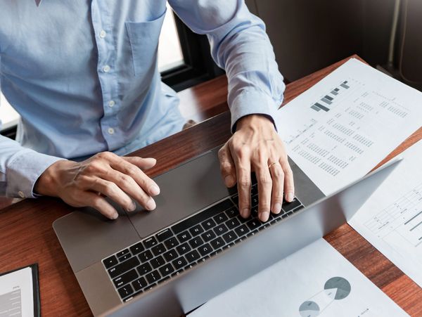 Person working on a laptop with financial documents and a calculator.