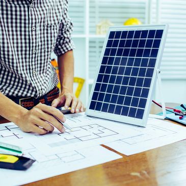 Person working on architectural plans with a small solar panel on the table.