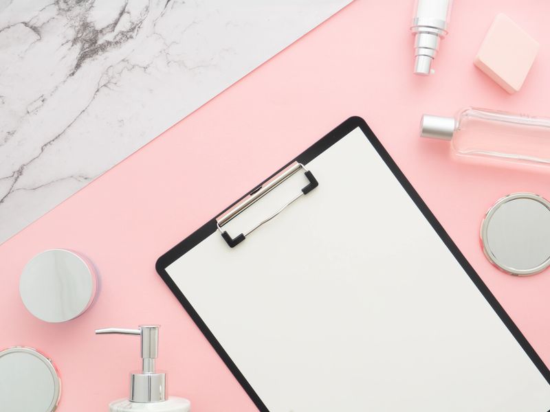 Beauty composition with a clipboard, curative cosmetics on pink background and marble texture imitation paper with copy space. Top view. Flat lay. Home feminine desk, Beauty blogger writer concept