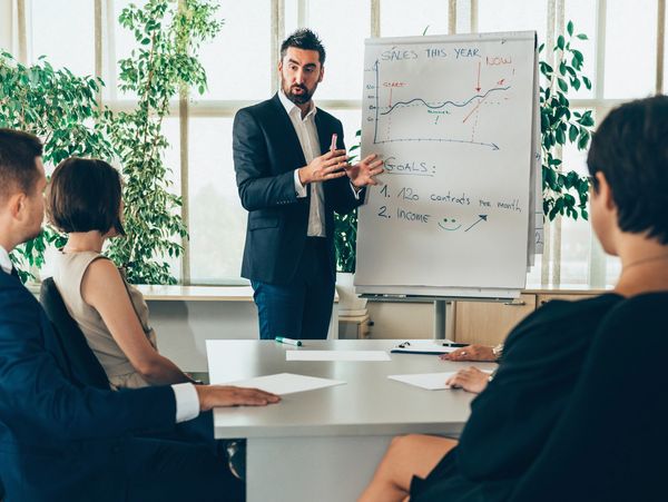 Businessman presenting sales goals to colleagues in a meeting room.