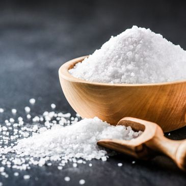 Coarse sea salt in a wooden bowl with a small scoop on a dark surface.