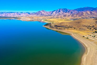A serene lake bordered by dry hills and mountains under a clear blue sky.