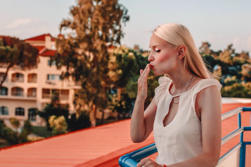 Beautiful stylish blonde woman in fashionable clothes posing on the balcony and blows a kiss.