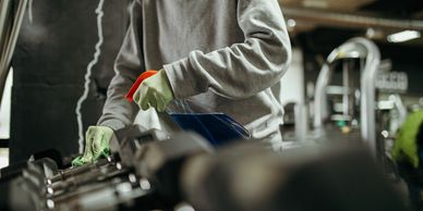 Person cleaning gym dumbbells with spray and cloth.