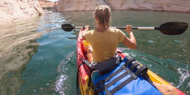 Person kayaking on calm water surrounded by rocky cliffs.