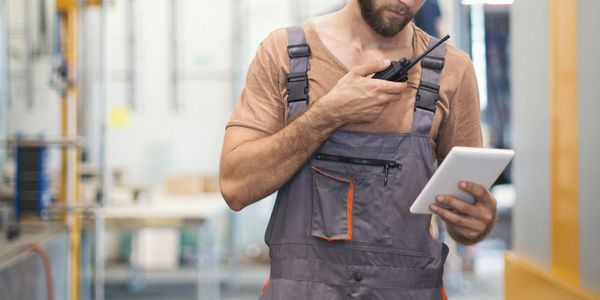Worker using tablet and walkie-talkie in industrial setting.