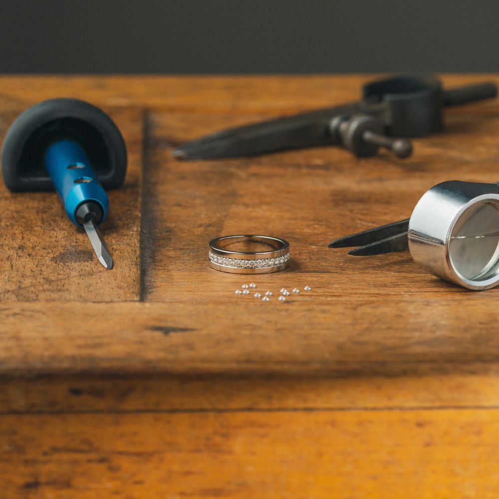 Jewelry tools and a diamond-studded ring on a wooden workbench.