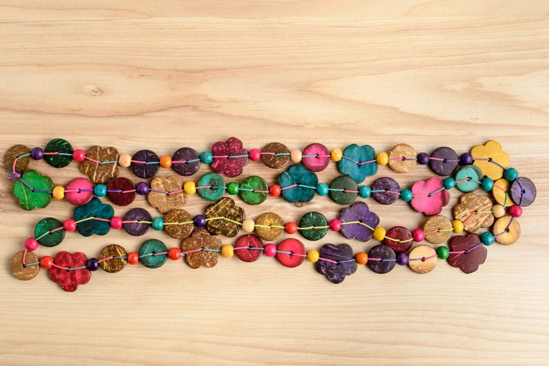 Multi coloured beards hand made from coconut shell flower and rounded pieces, traditional African decoration on a natural wooden background, side view, copy space