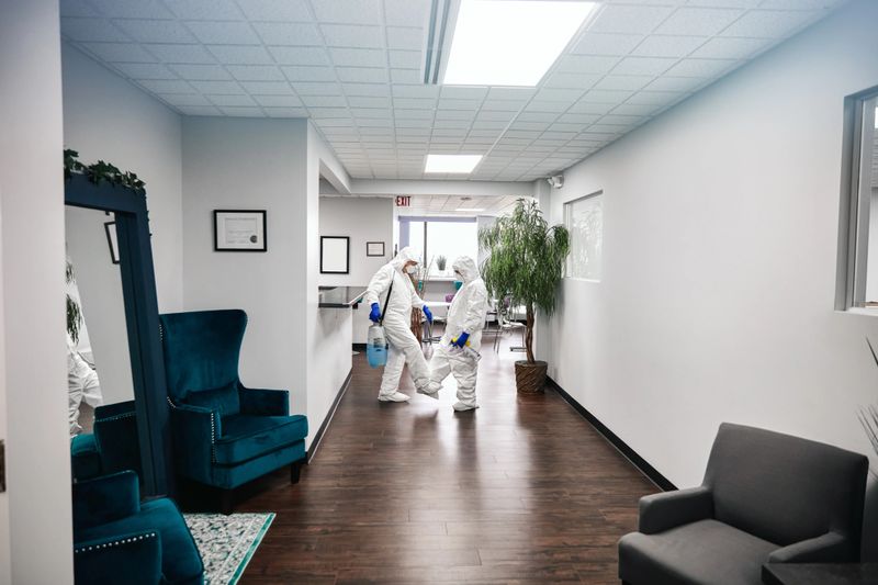 Two people in protective workwear cleaning and disinfecting offices.