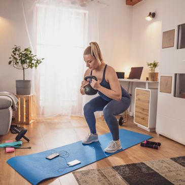 Woman exercising with kettlebell on a blue mat at home.