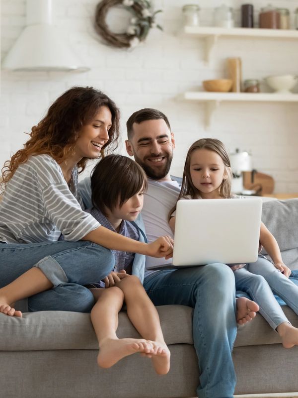 A happy family of four using a laptop together on a couch in a cozy kitchen.