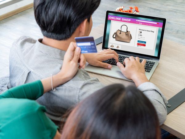 Couple shopping online for a women's handbag using a laptop and credit card.