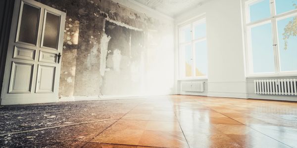 A room with one wall damaged and the other side freshly renovated with shiny wooden floor.
