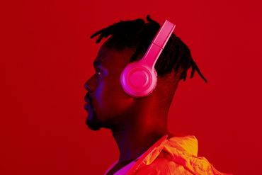 Man with pink headphones listening to music against red background.