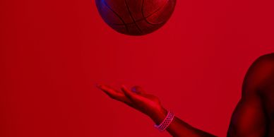 A person tossing a basketball against a red background.