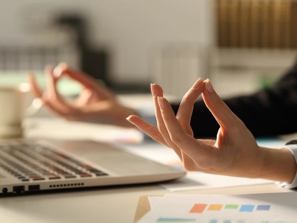 Person meditating with hands in a mudra pose near a laptop.
