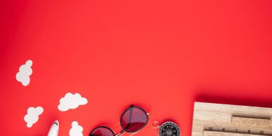Travel essentials including sunglasses and compass on red background.