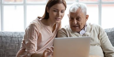 Young woman helps elderly man use a laptop at home.