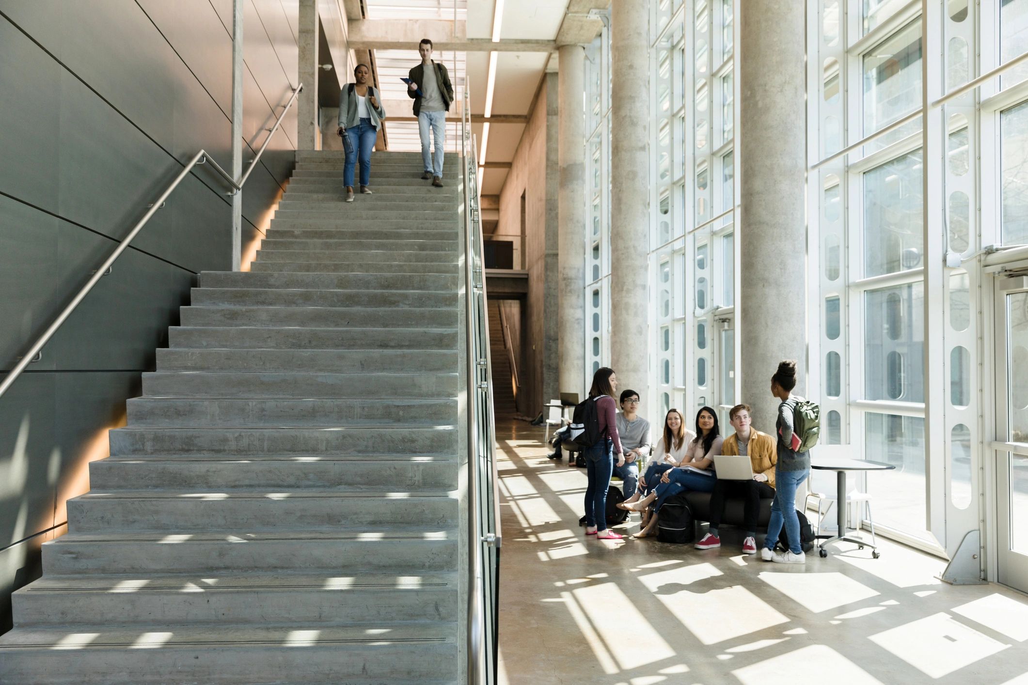 Students studying and walking in a modern building with large windows.