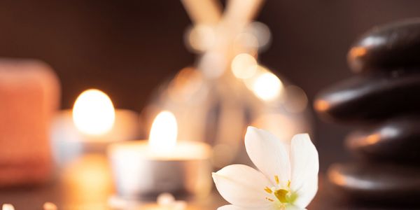 White flower with lit candles and stacked stones for a calming spa scene.