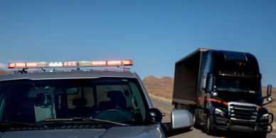 Police vehicle with flashing lights and a black truck on a desert road.