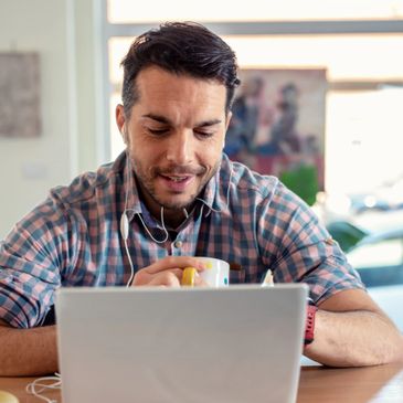 Man in checkered shirt video chatting with earbuds and holding a coffee mug.