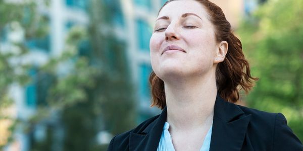 A woman enjoying a peaceful moment outdoors with eyes closed.