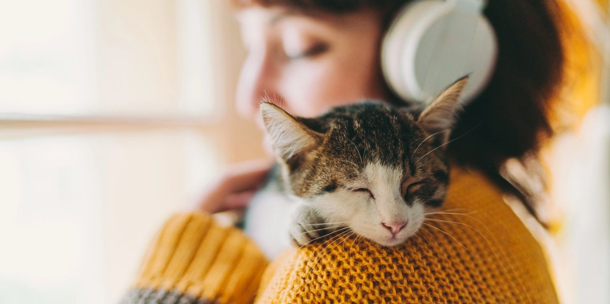 Young woman wearing headphones while snuggling a kitten on her shoulder.