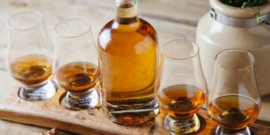Whiskey bottle and four glasses with whiskey on a wooden board.