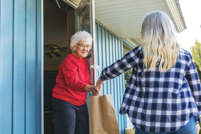 Young woman hands groceries to an elderly woman at her door.