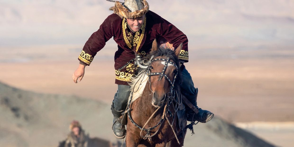 A man in traditional attire riding a horse with a joyful expression.