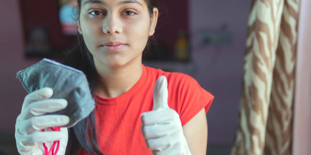 Young woman with gloves showing thumbs up and holding a mask.